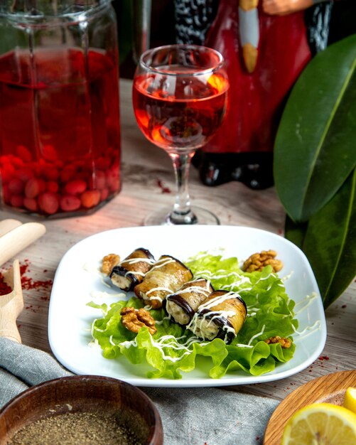 Vue de face aubergine roulée avec farce sur feuille de laitue aux noix et un verre de campot