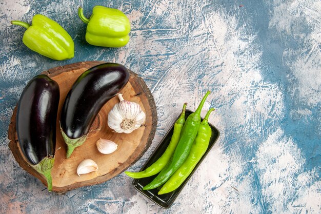 Vue de face aubergines ail sur planche de bois d'arbre poivrons piments verts chauds sur plaque noire sur fond bleu-blanc espace libre