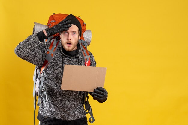 Vue de face de l'auto-stoppeur masculin agité avec des gants en cuir et sac à dos tenant du carton vierge