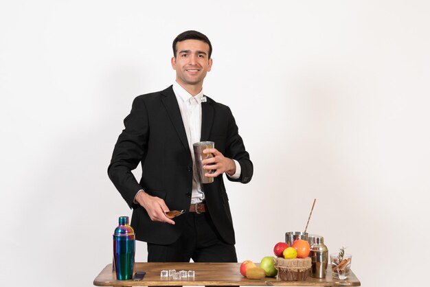 Vue de face barman masculin en costume travaillant avec des shakers et faisant un verre sur un bureau blanc club de nuit masculin bar à boissons dansant