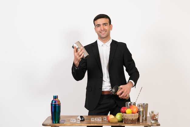 Vue de face barman masculin en costume travaillant avec des shakers et faisant un verre sur un bureau blanc nuit danse masculine boisson bar club