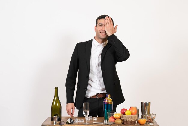 Vue de face barman masculin debout devant une table avec des boissons posant sur un mur blanc bar nuit club de boissons alcoolisées masculines