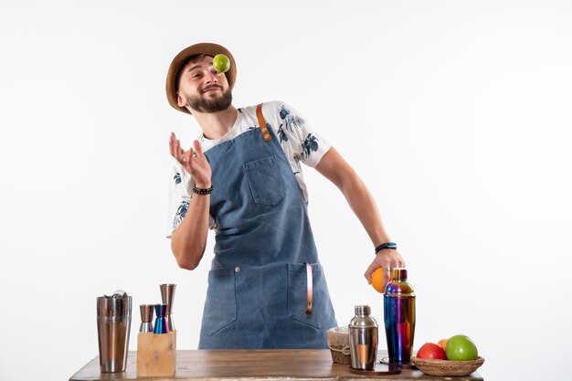 Vue de face barman masculin devant le bureau du bar jouant avec des fruits sur un mur blanc bar alcool travail de nuit club de boissons aux fruits