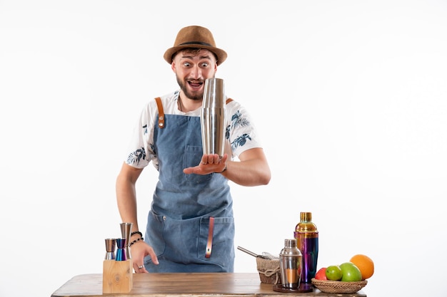 Vue de face barman masculin devant le bureau du bar préparer un verre sur un mur blanc bar travail d'alcool fruit club boisson de nuit