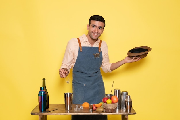 Photo gratuite vue de face barman masculin devant le bureau avec shakers et bouteilles faisant un verre sur un mur jaune club bar boire de l'alcool de nuit