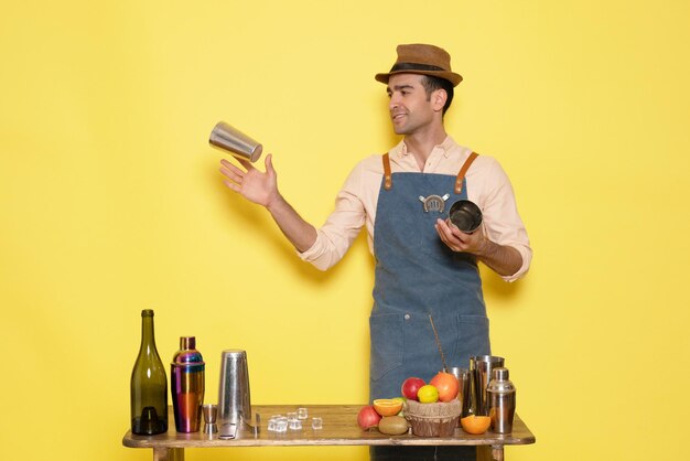 Vue de face barman masculin travaillant avec des shakers et faisant un verre sur un bureau jaune nuit un homme boit de l'alcool bar club