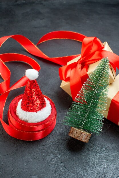 Vue de face de beaux cadeaux avec ruban rouge et sapin de Noël chapeau de père Noël sur une table sombre