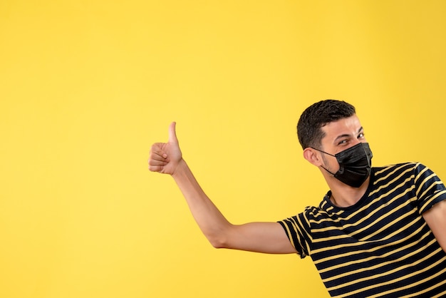 Vue de face bel homme au masque noir faisant le pouce vers le haut signe sur fond isolé jaune