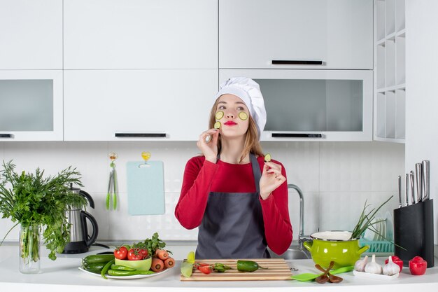 Vue de face belle femme chef en chapeau de cuisinier mettant des tranches de concombre sur son visage