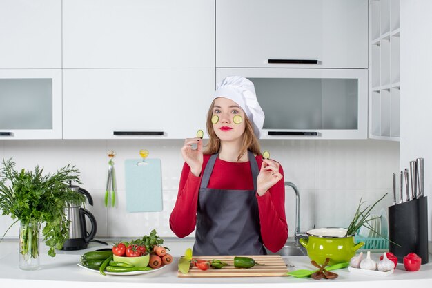 Vue de face belle femme chef en chapeau de cuisinier mettant des tranches de concombre sur son visage