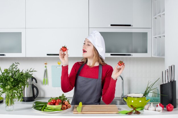 Vue de face belle femme cuisinier en tablier tenant des tomates