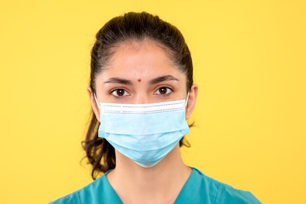 Vue de face belle femme médecin avec masque debout sur fond jaune