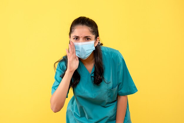 Vue de face belle femme médecin en uniforme disant quelque chose sur fond jaune