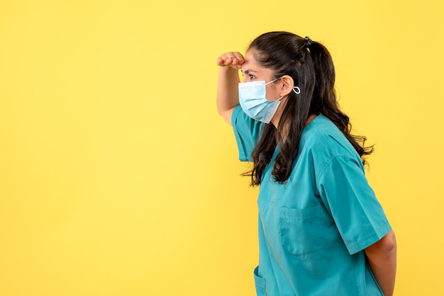 Vue de face belle femme médecin en uniforme observant sur fond jaune