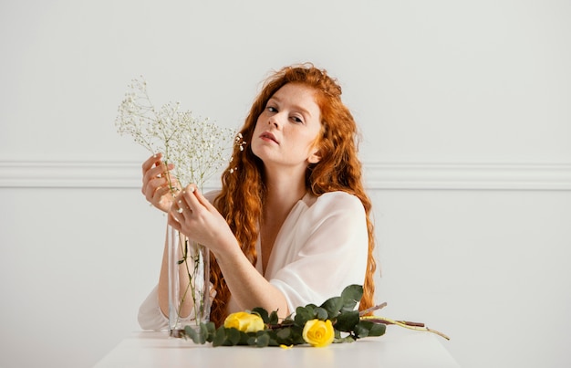 Photo gratuite vue de face de la belle femme posant avec des fleurs de printemps sur la table