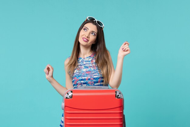 Vue de face belle femme se préparant pour des vacances avec un sac rouge sur un espace bleu clair