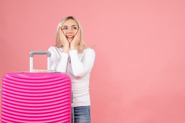 Vue de face belle femme avec valise rose mettant les mains sur sa joue