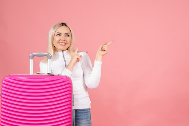 Vue de face belle femme avec valise rose pointant vers la gauche