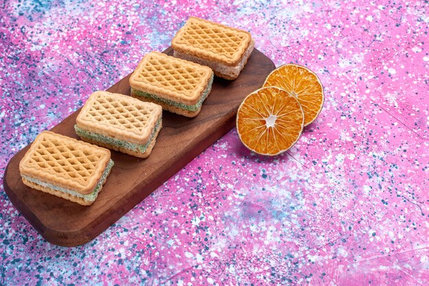 Vue de face biscuits gaufres avec garniture de crème aux fruits sur fond rose.