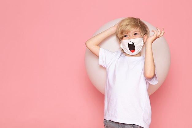 Photo gratuite une vue de face blond garçon souriant en t-shirt blanc et drôle de masque sur l'espace rose