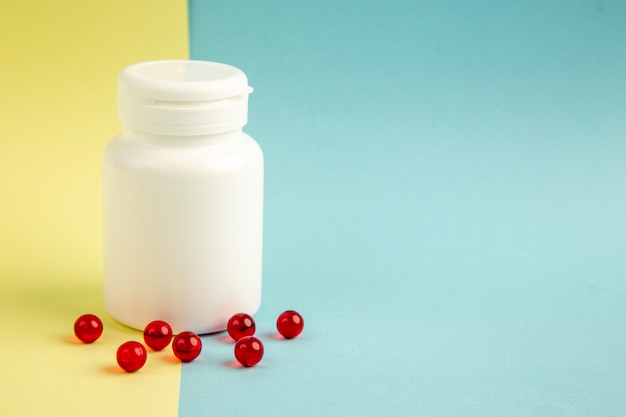 Vue de face boîte en plastique avec des pilules rouges sur fond jaune-bleu