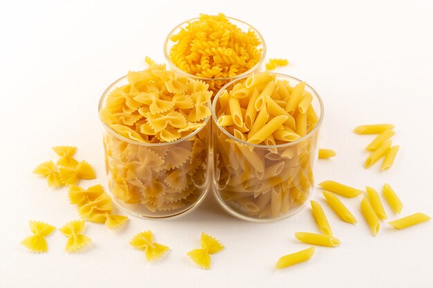 Une vue de face bols avec pâtes pâtes jaunes italiennes sèches à l'intérieur de bols en plastique transparent sur fond blanc repas italien