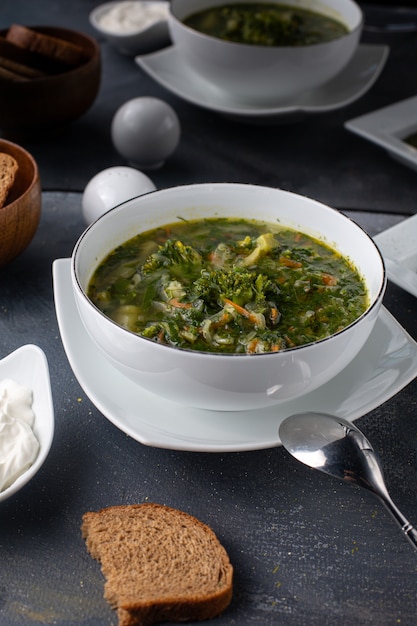 Photo gratuite une vue de face bortsch vert salé poivré avec des légumes et des miches de pain à l'intérieur de la plaque blanche repas liquide soupe