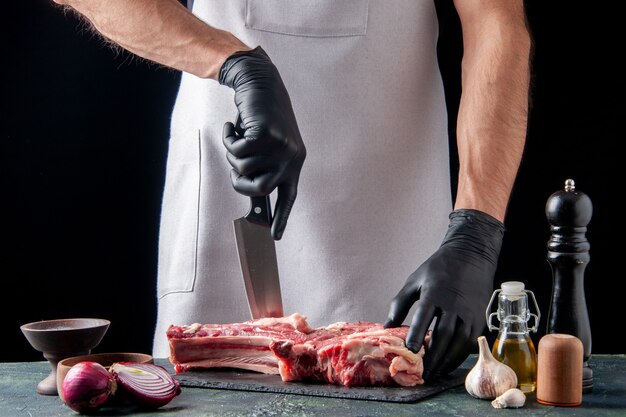 Vue de face boucher mâle coupant la viande sur une surface sombre