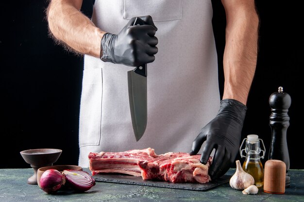 Vue de face boucher mâle coupant la viande sur une surface sombre