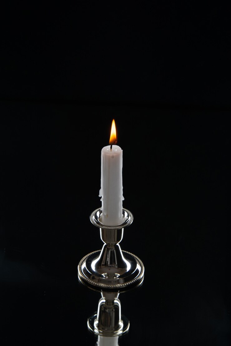Photo gratuit vue de face de la bougie allumée en support doré sur une surface sombre