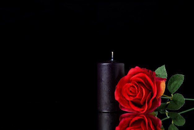 Vue de face de la bougie sombre avec une rose rouge sur une surface noire