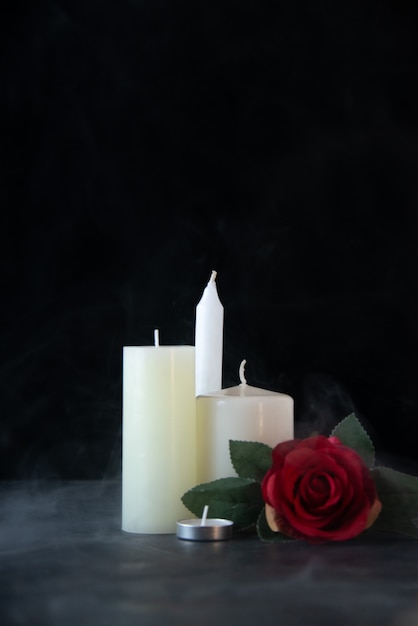 Vue de face de bougies blanches avec une rose rouge comme mémoire sur un mur sombre