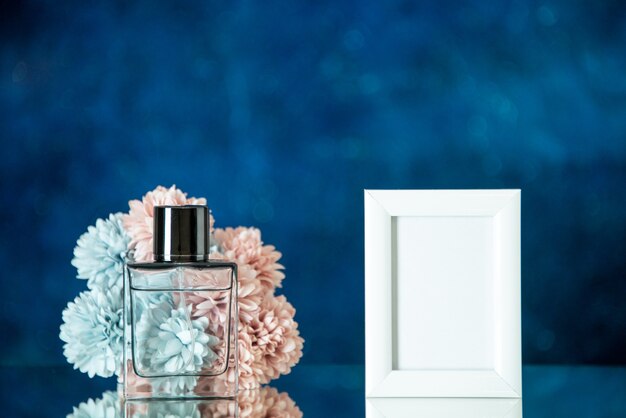 Vue de face bouteille de parfum petit cadre photo blanc fleurs sur fond bleu foncé