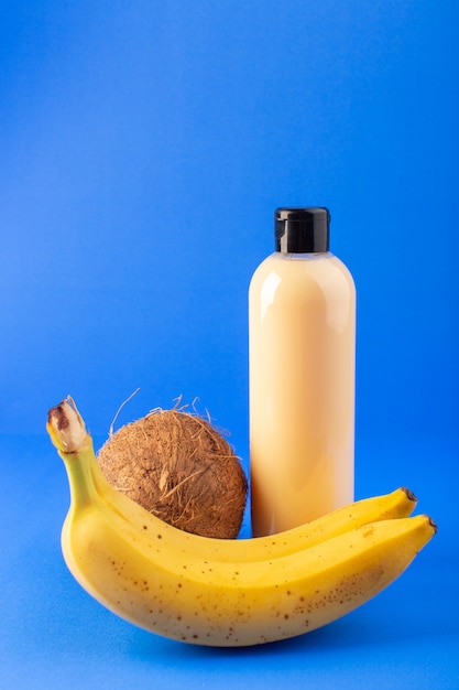 Une vue de face bouteille de shampooing en plastique de couleur crème peut avec capuchon noir isolé avec de la noix de coco et des bananes sur le fond bleu cheveux beauté cosmétiques