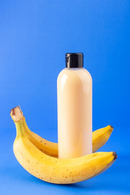 Une vue de face bouteille de shampooing en plastique de couleur crème peut avec capuchon noir isolé avec de la noix de coco et des bananes sur le fond bleu cheveux beauté cosmétiques