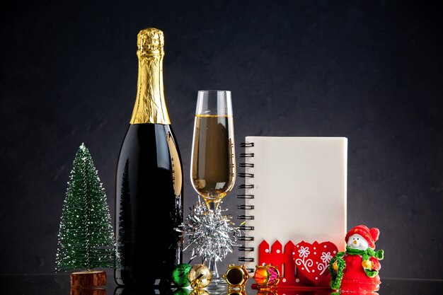 Vue de face bouteille de verre de champagne ornements de noël cahier mini arbre de noël sur une surface sombre