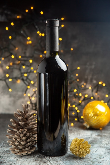 Photo gratuite vue de face d'une bouteille de vin rouge pour la célébration et de deux cônes de conifères sur fond sombre