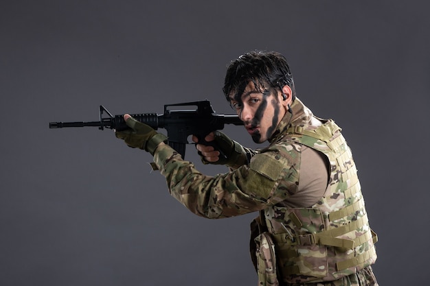 Vue de face brave soldat combattant en camouflage avec un mur sombre de mitrailleuse