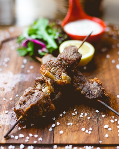 Vue de face brochette de viande sur des brochettes avec du sel et une tranche de citron sur la planche