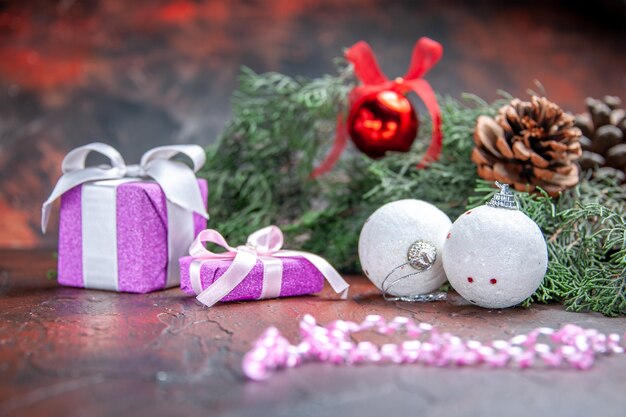 Vue de face cadeaux de Noël branches d'arbres de pin jouets de boule de Noël sur fond isolé rouge foncé photo de Noël