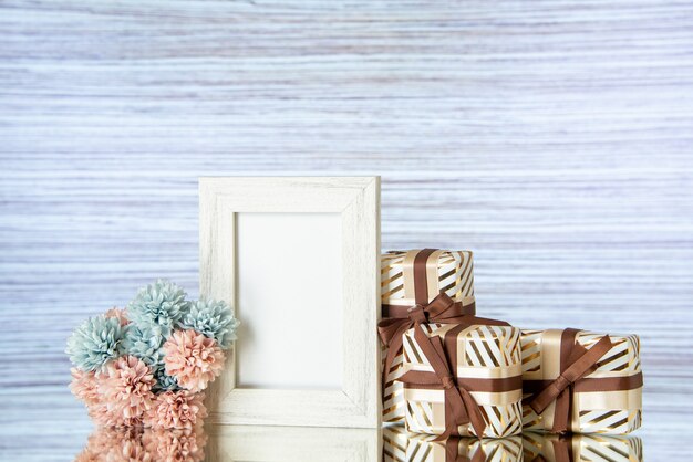 Vue de face des cadeaux de la Saint-Valentin attachés avec un cadre photo blanc de fleurs de ruban marron réfléchi sur un miroir