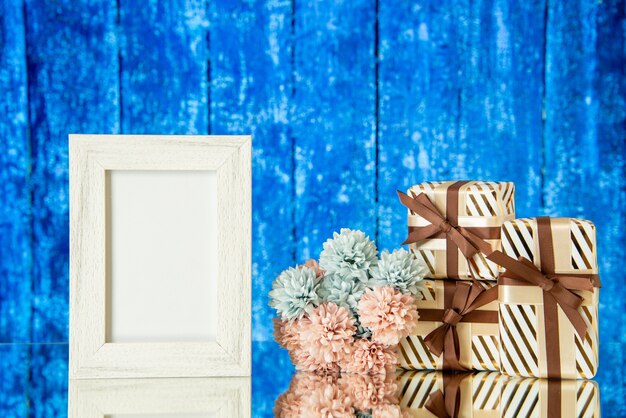 Vue de face des cadeaux de vacances de cadre photo blanc reflétés sur un miroir avec un fond en bois bleu