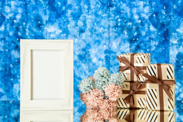 Photo gratuite vue de face cadre photo blanc cadeaux de vacances fleurs reflétées sur miroir avec un fond bleu galaxie