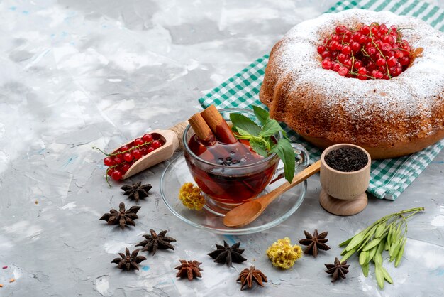 Une vue de face de canneberges rouges fraîches aigre-doux et moelleux avec du thé gâteau rond et de la cannelle sur le bureau blanc fruit berry
