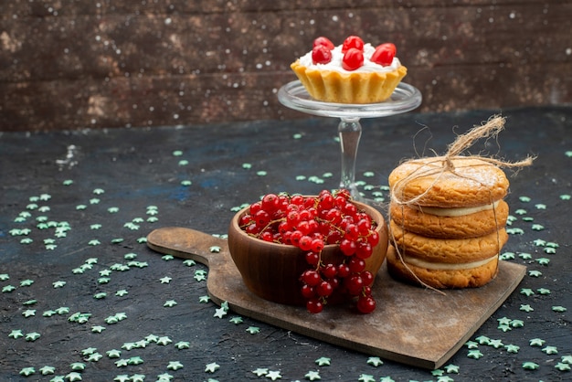 Vue de face de canneberges rouges fraîches à l'intérieur du bol avec garniture de crème biscuits sandwich sur la surface sombre sucre gâteau sucré