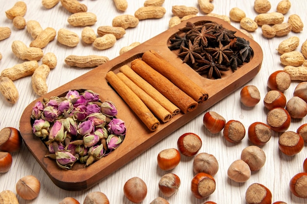 Vue de face de la cannelle fraîche avec des fleurs et différentes noix sur la couleur des plantes à fleurs de bureau blanc