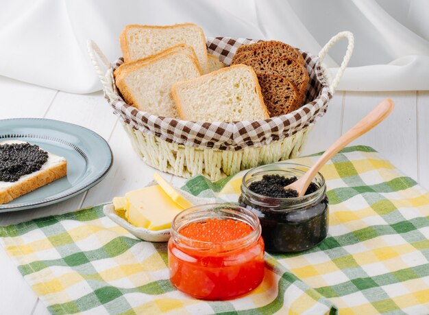 Vue de face caviar rouge et noir dans des bocaux en verre avec du beurre et du pain dans un panier