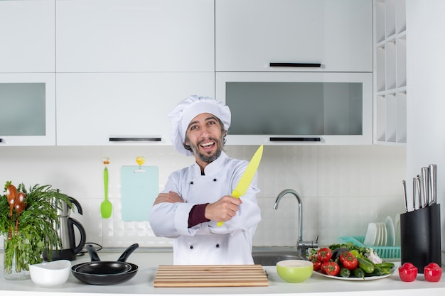 Vue de face chef masculin en uniforme brandissant un couteau croisant les mains sur une cuisine moderne