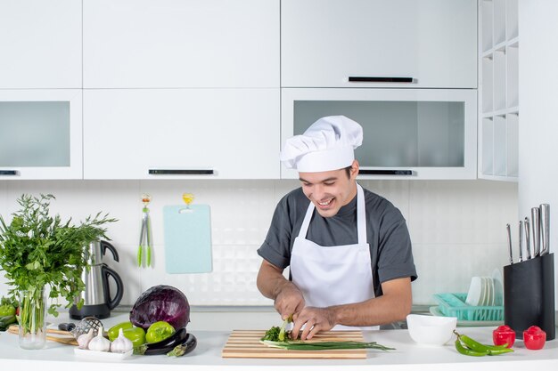 Vue de face chef masculin en uniforme de coupe de légumes verts sur planche de bois