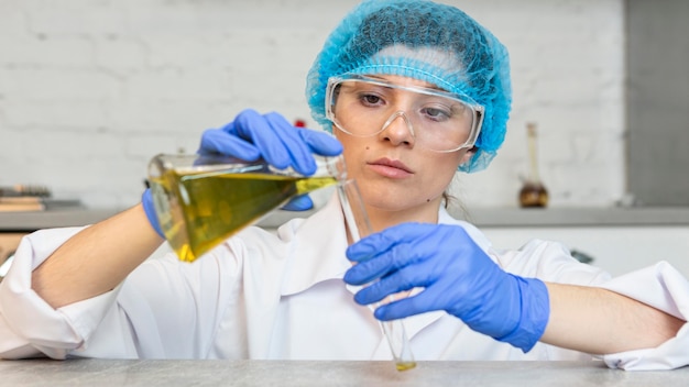 Vue de face d'une chercheuse avec des lunettes de sécurité et un filet à cheveux faisant des expériences scientifiques